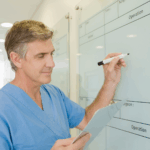 A photo of a man in blue medical scrubs writing on a white board with a dry-erase marker. Used for GF 110 EraseMark Pro.