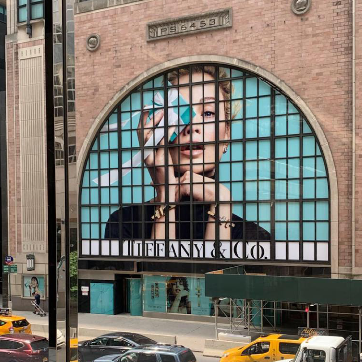 GF 202_Image_square I photo of the Tiffany & Co storefront in New York City. There is an image of a blonde woman on a solid, Tiffany Blue background, holding a small Tiffany Blue jewelry gift box over her right eye (the viewer's left side). The image has been printed on GF 202 and applied to the windows.
