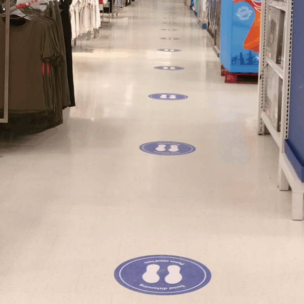 A photo of a hallway in a clothing store with purple circles on the ground with the outlines of the bottoms of shoes in solid white. These circles are adhered to the tile floor and printed on GF 212.