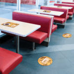 Photo of what appears to be a 50s style diner with red vinyl booth seats and and light-colored tables with metal trim. There are yellow decals on the floor and tabletops. The decals are printed on GF 213.