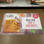 A photo of the floor of a store in what appears to be the dog food section. There is a decal on the floor that contains a photo of the Purina Beyond brand of dogfood in the Simply 9 White Meat Chicken and Barley flavor. The dog food back is white on top with yellow on the bottom and an illustration of a chicken. To the right of this is a white box on a photo of a wooden floor that says, "New Look," in black text, and, "Same 9 Ingredients" in red text." There is a smaller red circle above this text that reads, "New lower price," in white text. This floor decal is printed on GF 217.
