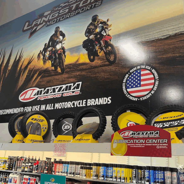 Photo of the inside of an auto parts store. There are various cans on the shelves and tires on display. On the wall above everything is a graphic containing a photo of riders on dirt bikes riding along the ocean, along with various logos. The wall graphic was printed on GF 231.