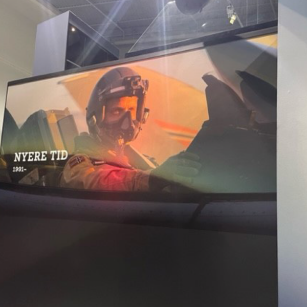 A photo of what appears to be the inside of a museum. There is a display with a large image of a fighter pilot in the cockpit of his jet. This image was printed on GF 238.