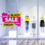 A photo of mannequins in the window of a clothing store. There is a pink and yellow graphic on the window that reads, "Black Friday Super Sale -50% off." The graphic is printed on GF 261.