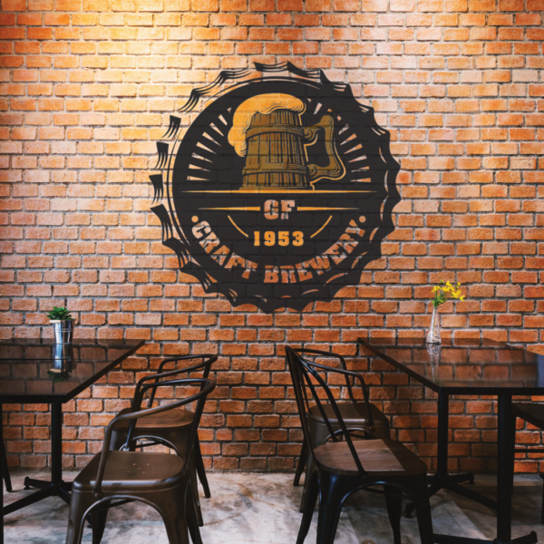 A photo of the inside of a restaurant. There are black metal chairs and tables. There is a brick wall with a black decal. It is shaped like a bottle-cap with the text, "GF 1953 Craft Brewery," underneath an illustration of a pint of bear in an old wooden cup and metal handle. The decal is printed on GF 287.