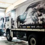 A phot of white trucks in a garage for hauling products. The trucks have black and white decals of a car on the side. The decal is printed with Arlon DPF 4600