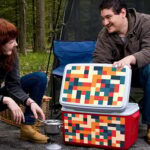 A man and a woman on a picnic in the woods. There is a multi-colored checker printe on a red and white cooler. The checker printed is printed on Arlon DPF 8200