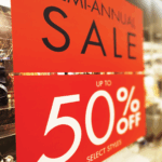A photo of a sign hanging in a clothing store. It is red with black text that reads, "Semi-annual sale," on top and white text that reads, "Up to 50% off select styles" on the bottom. The sing was printed on GF 223.
