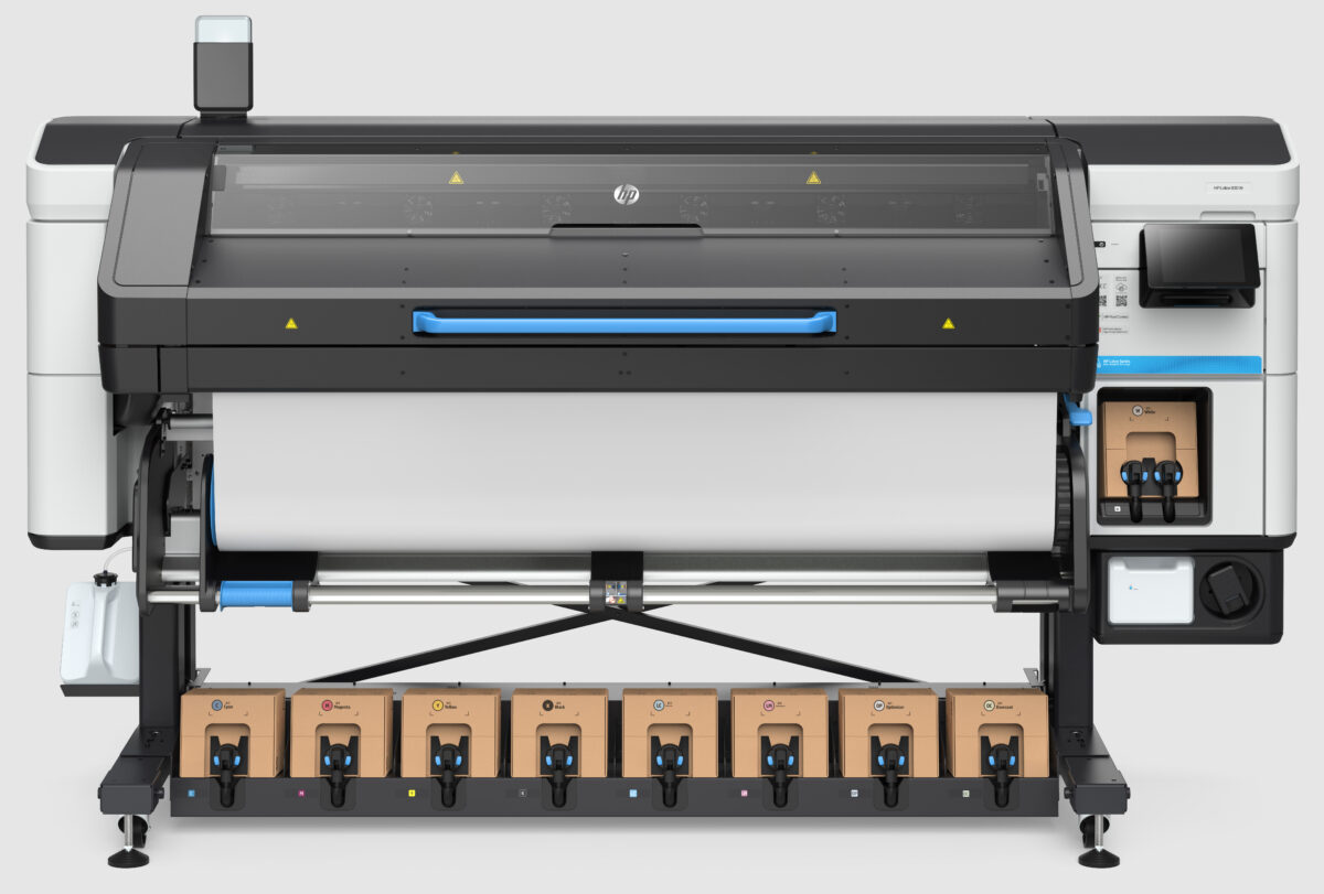 A photo of the HP Latex 830 W printer from the front. There is a roll of paper loaded for printing. The ink can be seen installed on the bottom.