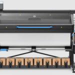 A photo of the HP Latex 830 W printer from the front. There is a roll of paper loaded for printing. The ink can be seen installed on the bottom.