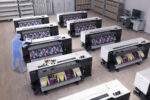 Mock-up of a room containing eight Epson SureColor F9570 printers. A blue image of a person standing among them for scale.