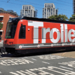 A photo of a trolley/light rail in a city. It is red with the word, "Trolley," written in large, white text. The outside of the trolley is a wrap printed on GF 209AE.