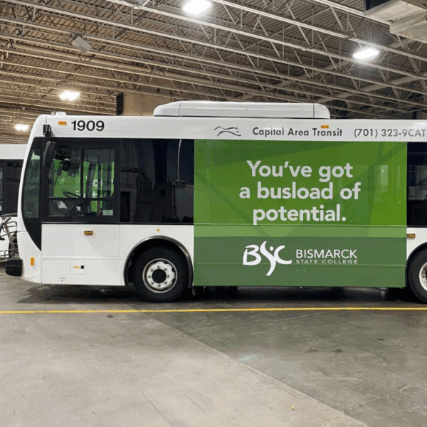 A photo of a white city bus with a green graphic on the side. It has white, sans-serif text that reads, "You've got a busload of potential," With the logo for Bismark State College underneath. The graphic was printed on GF 232.