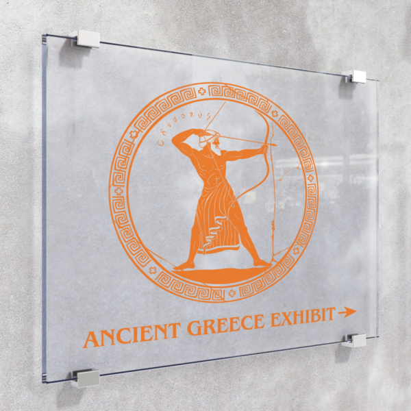 A photo of a grey wall with four metal clips attached to the wall. The clips are holding a piece of clear glass with an orange graphic on it. The graphic is a circle outlined with various patterns and an ancient greek man aiming a bow and arrow. Below is orange text that reads, "Ancient Greece Exhibit," with an arrow pointing to the right. The orange graphic is printed on GF 255.