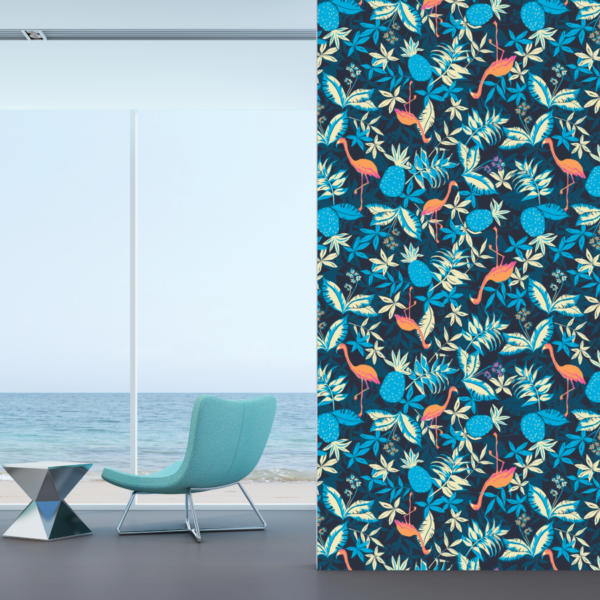A photo from inside a house overlooking a beach and the ocean. There is a minimalistic light teal chair and a silver geometric side table. in the foreground is a wall with dark wallpaper covered in flamingos, pineapples, and ferns, all in shades of teal, green, navy blue, and orange. The wallpaper is printed on GF 262HTR.