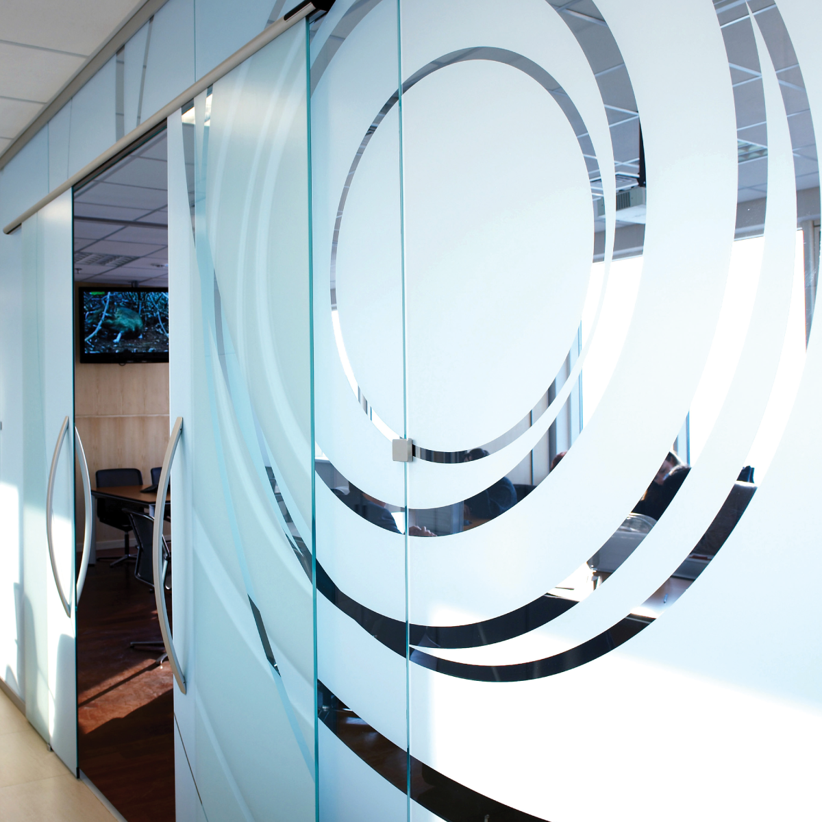 790AE_Print-N-Privacy_Image_square A photo of of a glass wall of a conference room. The wall is covered in a frosted opaque white with curved lines cut out of it. The frosted design was printed on GF 790AE.
