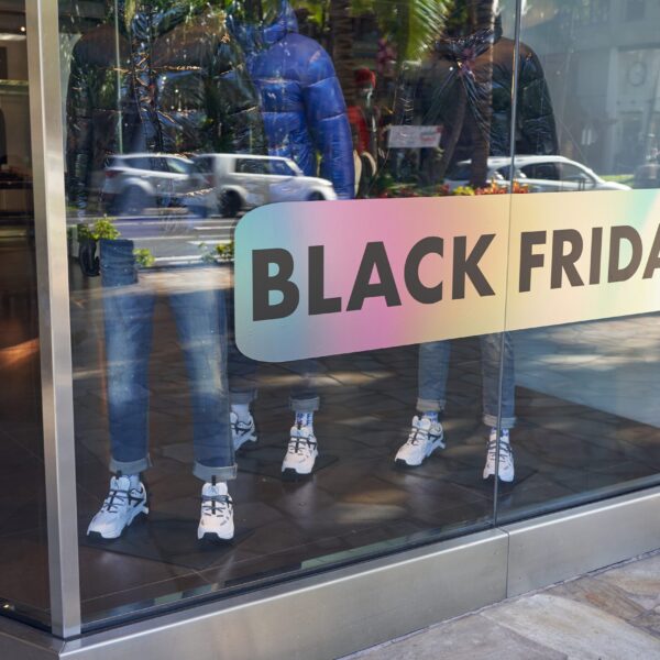 A photo of the front window of a clothing store along a busy street. There are mannequins wearing jeans and winter coats inside. There is a metalic decal with rainbow colors and in large words it reads, "BLACK FRIDAY," in all caps. The decal was printed on GF 364OP.