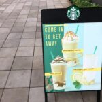 A photo of a Starbucks sign on a black A-frame sitting on a sidewalk. The sign contains photos of various beverages available with the text, "Come in to get away." The sign was printed on GF 365.