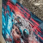 Photo of a concrete wall with a futuristic illustation of a woman wearing a white and blue helmet with wires attached. There are red and blue lights in the background. This image was printed on GF 885AE.