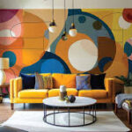 Image of a living room with a yellow couch, white and black coffee table, and white lights on black cables hanging from the ceiling. The wall is covered in an abstract mural with shaldes of blue, orange, yellow, and red with black lines. The mural is printed on 2502 WallBliss Spay & Stick